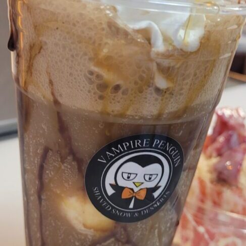 A close-up of a creamy iced coffee with chocolate drizzle in a plastic cup.