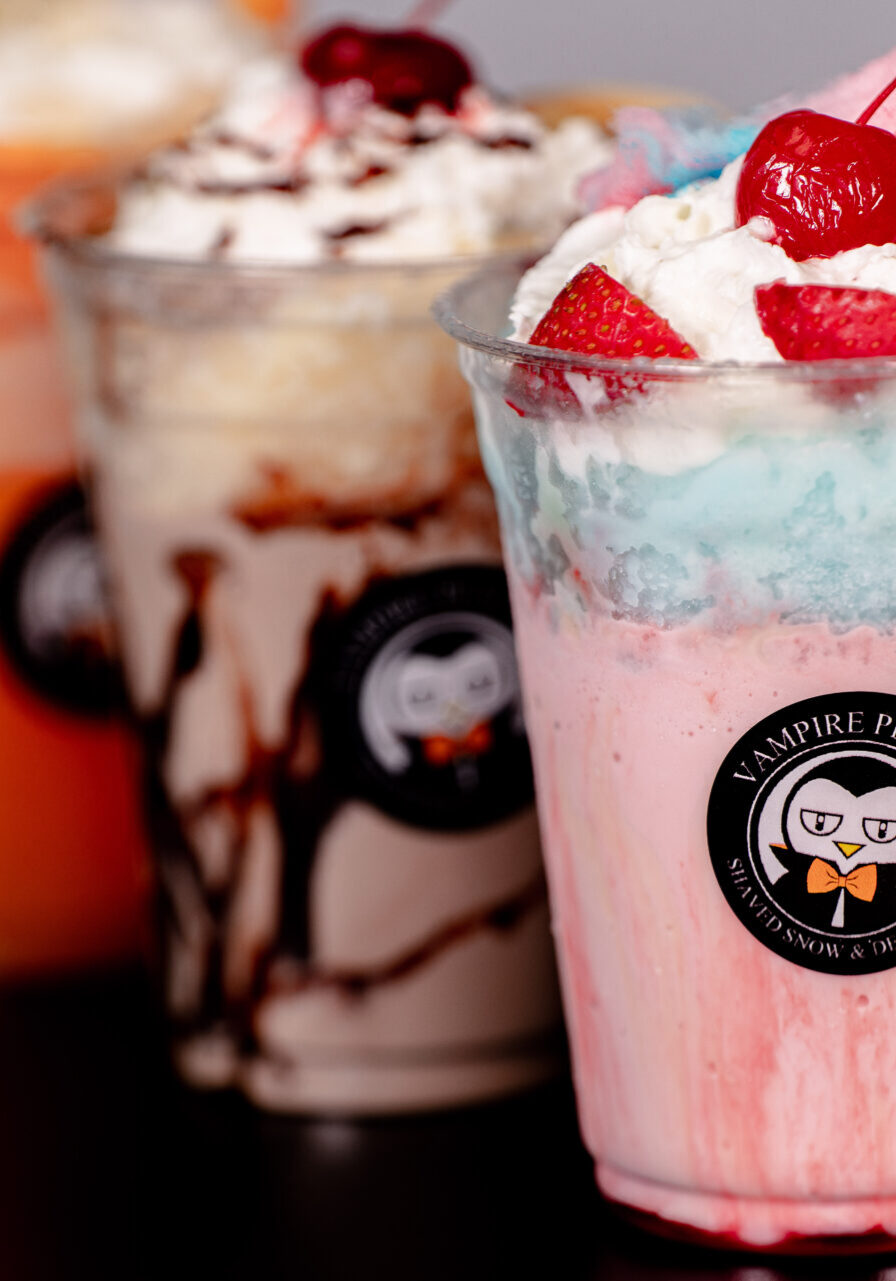 Three colorful milkshakes with whipped cream and toppings on a table.